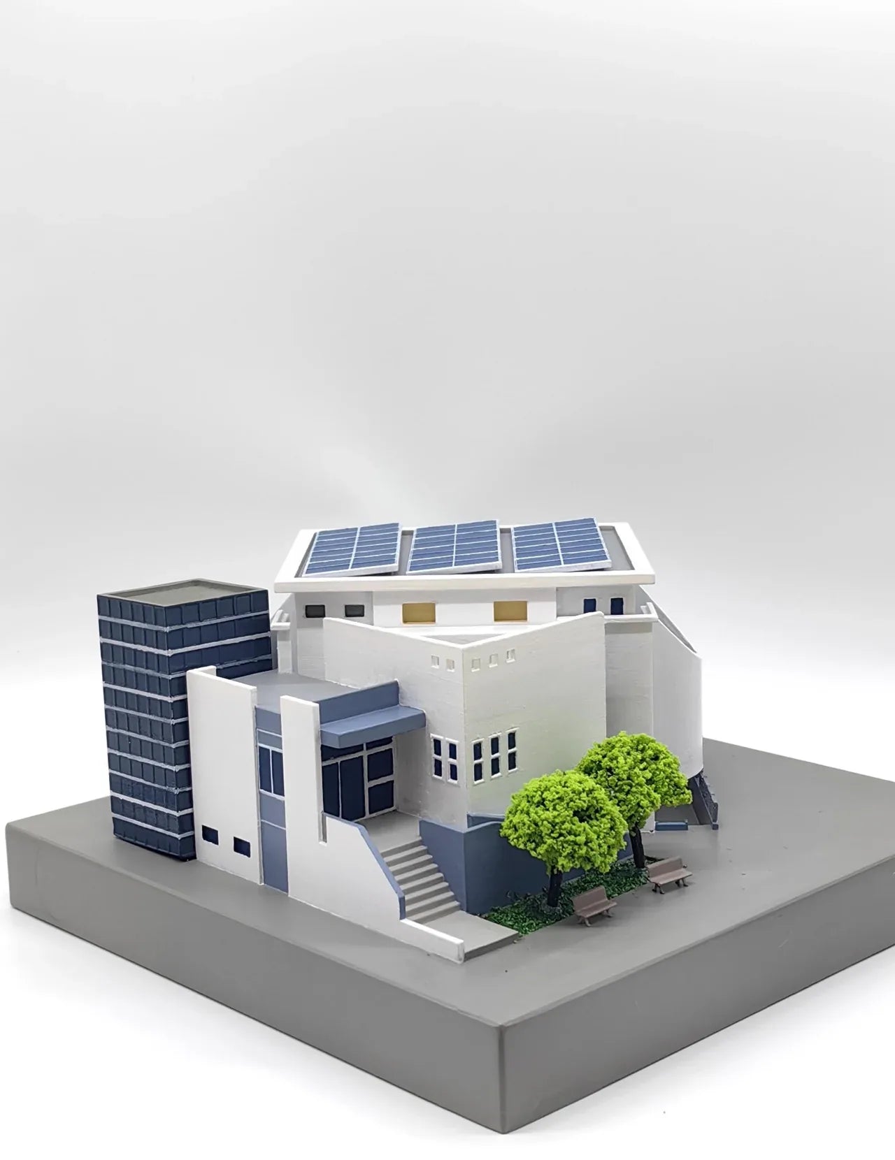 Completed modern architectural model with curved white walls, a blue glazed tower, rooftop solar panels and miniature trees.