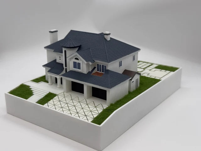 Finished white residence model with a detailed grey roof, columns, a patterned driveway and green lawn on a white base.