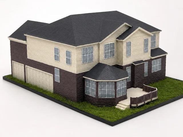 Completed model of a two-story home with a brick lower story, cream lap siding, a bay window, a railed back deck and a three-car garage on a lawn base.